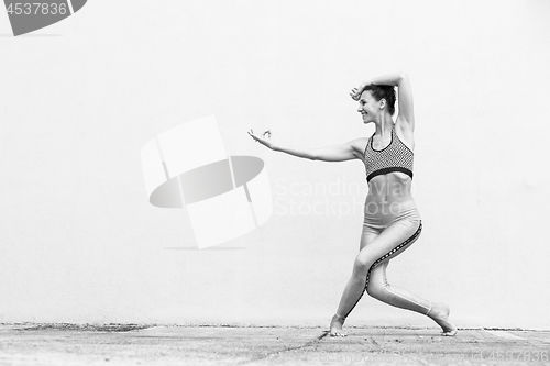 Image of Fit sporty active girl in fashion sportswear doing yoga fitness exercise in front of gray wall, outdoor sports, urban style. Black and white photo.