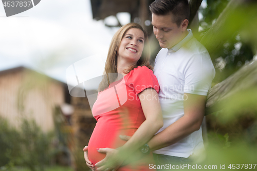 Image of Young happy pregnant couple hugging at countryside by hayrack.