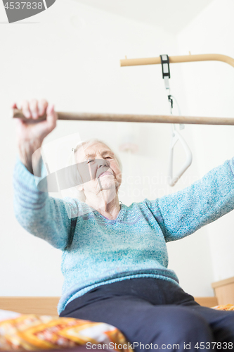 Image of Elderly 96 years old woman exercising with a stick sitting on her bad.