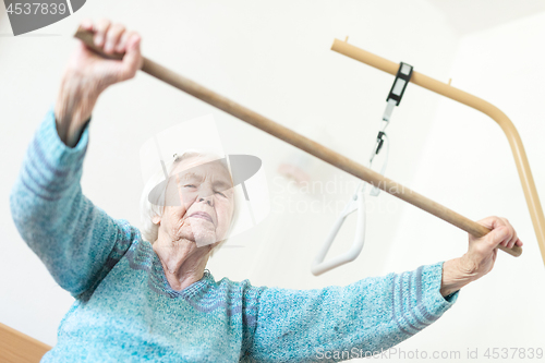 Image of Elderly 96 years old woman exercising with a stick sitting on her bad.