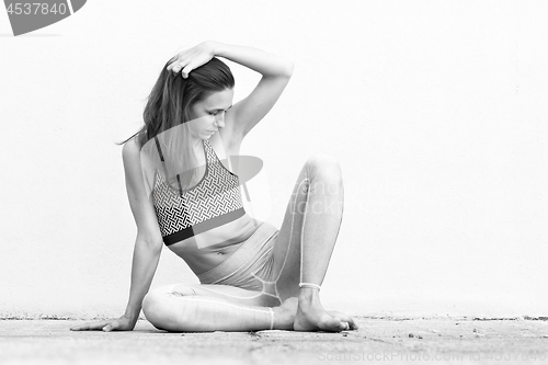 Image of Fit sporty active girl in fashion sportswear sitting on the floor in front of gray wall. Black and white photo.