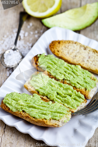 Image of Croutons with avocado guacamole on white plate closeup on rustic