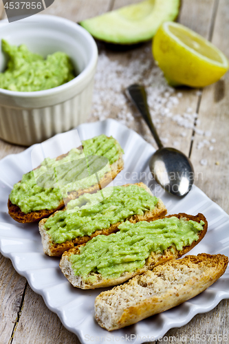 Image of Toasts with avocado guacamole on white plate closeup on rustic w