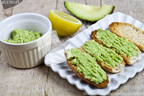 Image of Crostini with avocado guacamole on white plate closeup on rustic