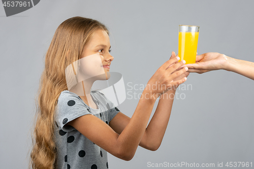 Image of A girl with two hands takes a glass of juice from the hand of another person