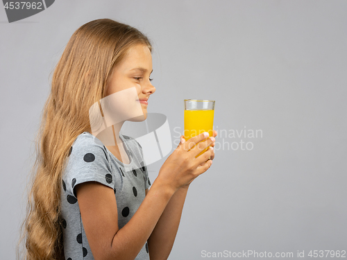 Image of A girl holds a glass of juice in her hands with two hands, profile view