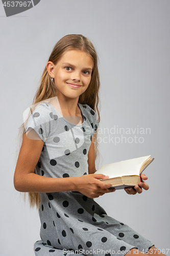 Image of A girl of ten years distracted from reading a book and happily looked into the frame