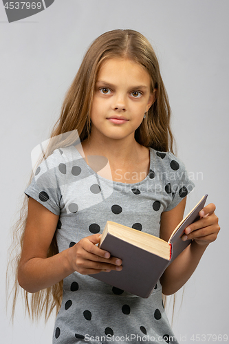 Image of Beautiful ten year old girl reads a book and looks into the frame