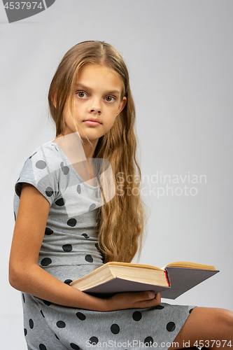 Image of A girl of ten years distracted from reading a book and looked at the frame