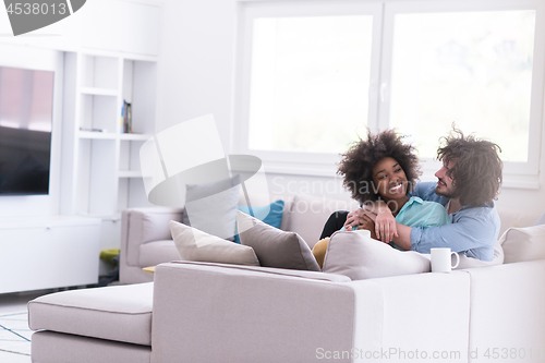 Image of multiethnic couple sitting on sofa at home drinking coffe