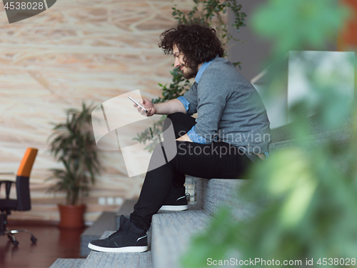 Image of Young casual businessman holding smartphone