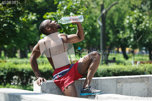 Image of Athlete resting and drinking water after exercises at stadium