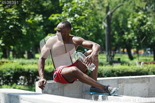 Image of Athlete resting and drinking water after exercises at stadium