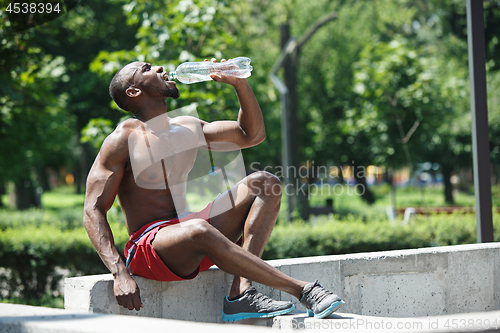 Image of Athlete resting and drinking water after exercises at stadium