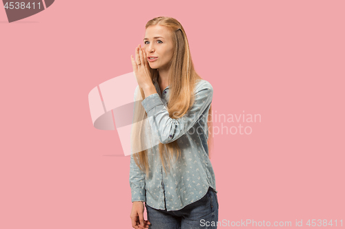 Image of The young woman whispering a secret behind her hand over pink background