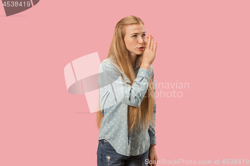 Image of The young woman whispering a secret behind her hand over pink background