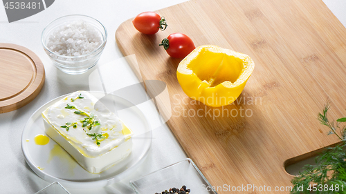 Image of Fresh cheese, peppers and tomatoes on a wooden board on a white kitchen table. Ingredients for salad.