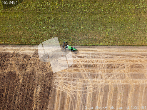 Image of Panoramic view of tractor plowing the soil after harvesting on the field. Top view from drone.