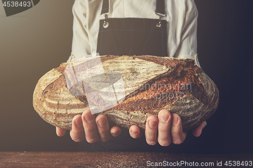 Image of Baker\'s hands hold an oval bread.