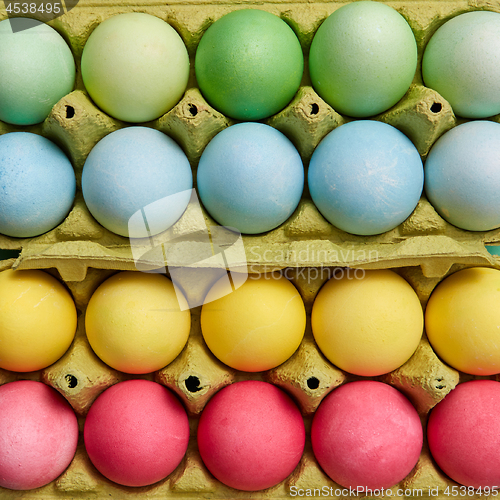 Image of Different colored painted Easter eggs in yellow cardboard boxes. Creative Easter pattern as layout. Flat lay