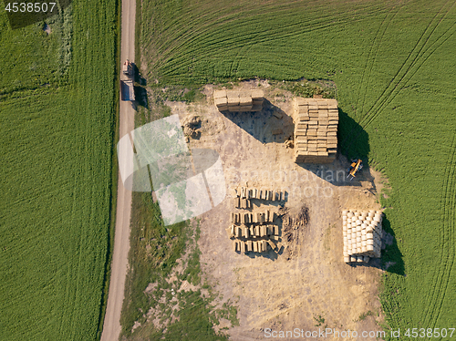 Image of Aerial view from drone into area with stacks of straw after harvesting the grain and dirty road with tractor on it.