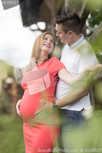 Image of Young happy pregnant couple hugging at countryside by hayrack.