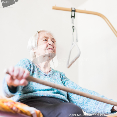 Image of Elderly 96 years old woman exercising with a stick sitting on her bad.