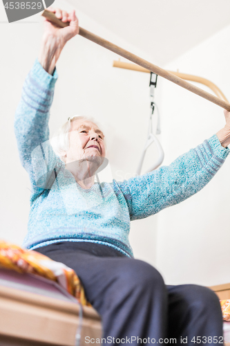 Image of Elderly 96 years old woman exercising with a stick sitting on her bad.