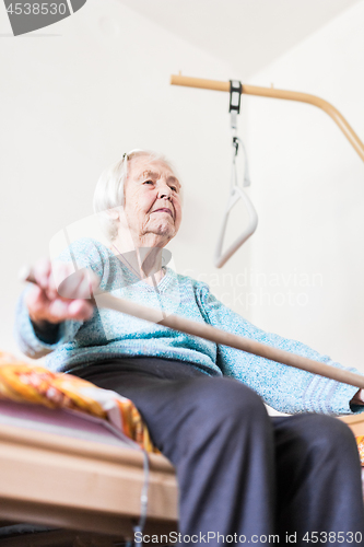 Image of Elderly 96 years old woman exercising with a stick sitting on her bad.