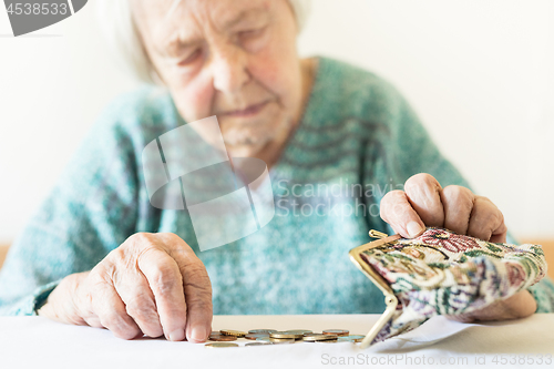 Image of Concerned elderly woman sitting at the table counting money in her wallet.