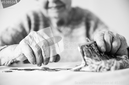 Image of Detailed closeup photo of unrecognizable elderly womans hands counting remaining coins from pension in her wallet after paying bills. Black and white image.