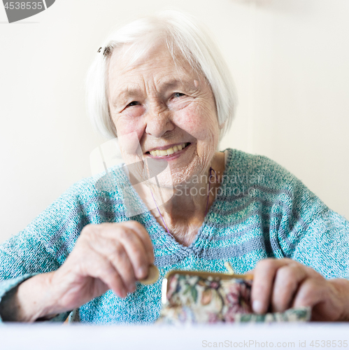 Image of Cheerful elderly 96 years old woman sitting at table at home happy with her pension savings in her wallet after paying bills.