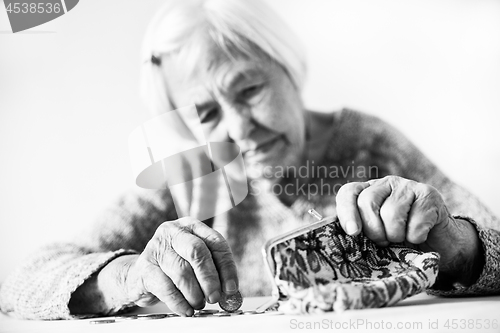 Image of Concerned elderly woman sitting at the table counting money in her wallet. Black and white photo.