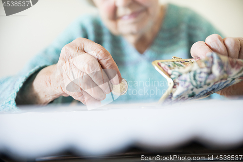 Image of Detailed closeup photo of unrecognizable elderly womans hands counting remaining coins from pension in her wallet after paying bills.