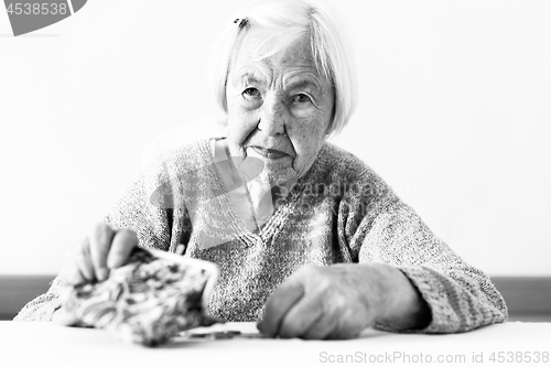 Image of Concerned elderly woman sitting at the table counting money in her wallet. Black and white photo.