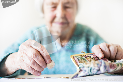 Image of Concerned elderly woman sitting at the table counting money in her wallet.