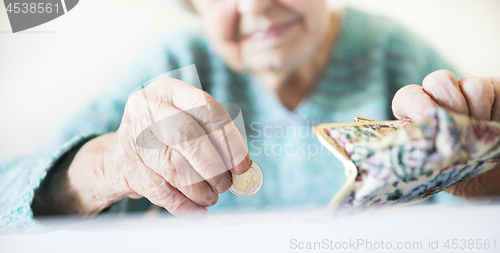 Image of Detailed closeup photo of unrecognizable elderly womans hands counting remaining coins from pension in her wallet after paying bills.