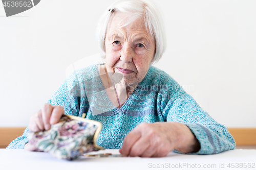 Image of Concerned elderly woman sitting at the table counting money in her wallet.