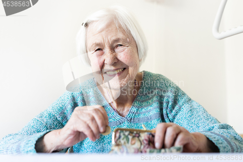 Image of Cheerful elderly 96 years old woman sitting at table at home happy with her pension savings in her wallet after paying bills.