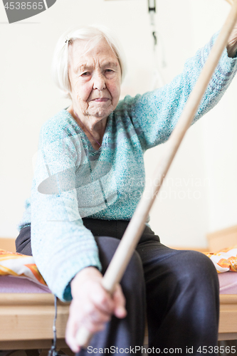 Image of Elderly 96 years old woman exercising with a stick sitting on her bad.
