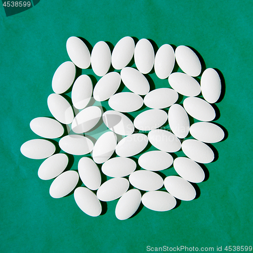 Image of White pills group on teal green background. 