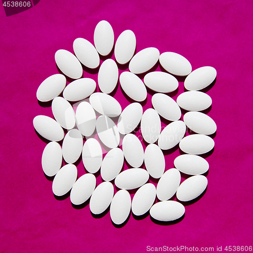 Image of White pills group on magenta background. 