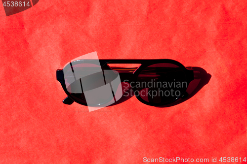 Image of Fashionabls black sunglasses with shadow on red background. 