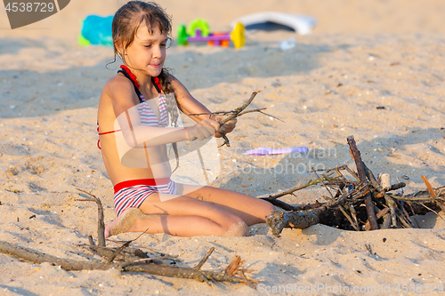 Image of Girl breaks brushwood for a bonfire on a sandy beach