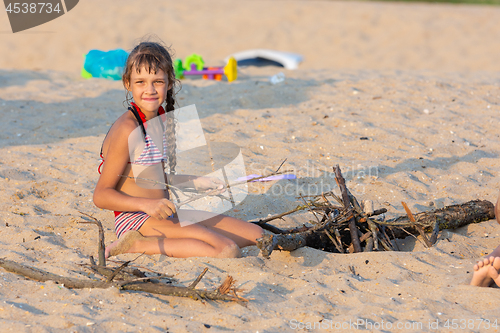Image of Girl breaks brushwood for a bonfire on a sandy beach and looked into the frame