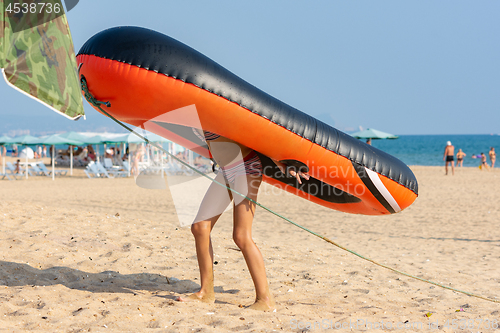 Image of Teen girl drags on her back a large inflatable boat on a sandy beach