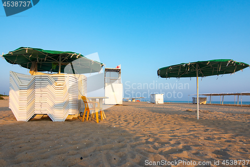 Image of Folded sun loungers and an empty lifeguard post on a deserted sandy beach at sunset