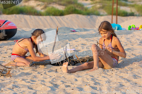 Image of Two girls in the evening on the beach prepare a place for a fire