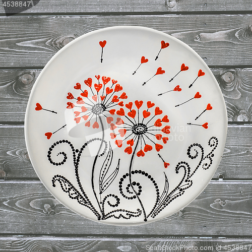 Image of Decorative ceramic plate, hand painted with acrylic paints on a wooden background. A square photo closeup.