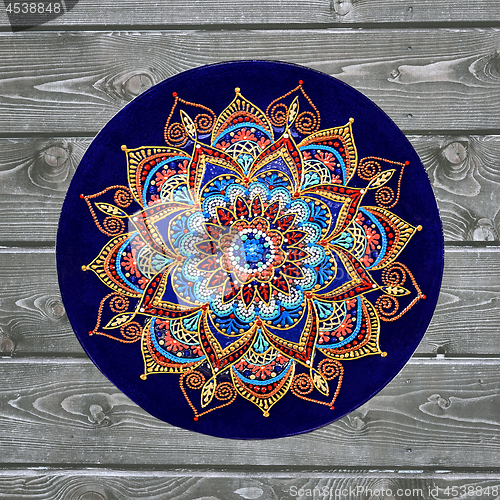 Image of Decorative ceramic plate, hand painted with acrylic paints on a wooden background. A square photo closeup.